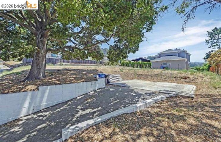 Backyard with a large shade tree, concrete retaining wall, and paved patio.