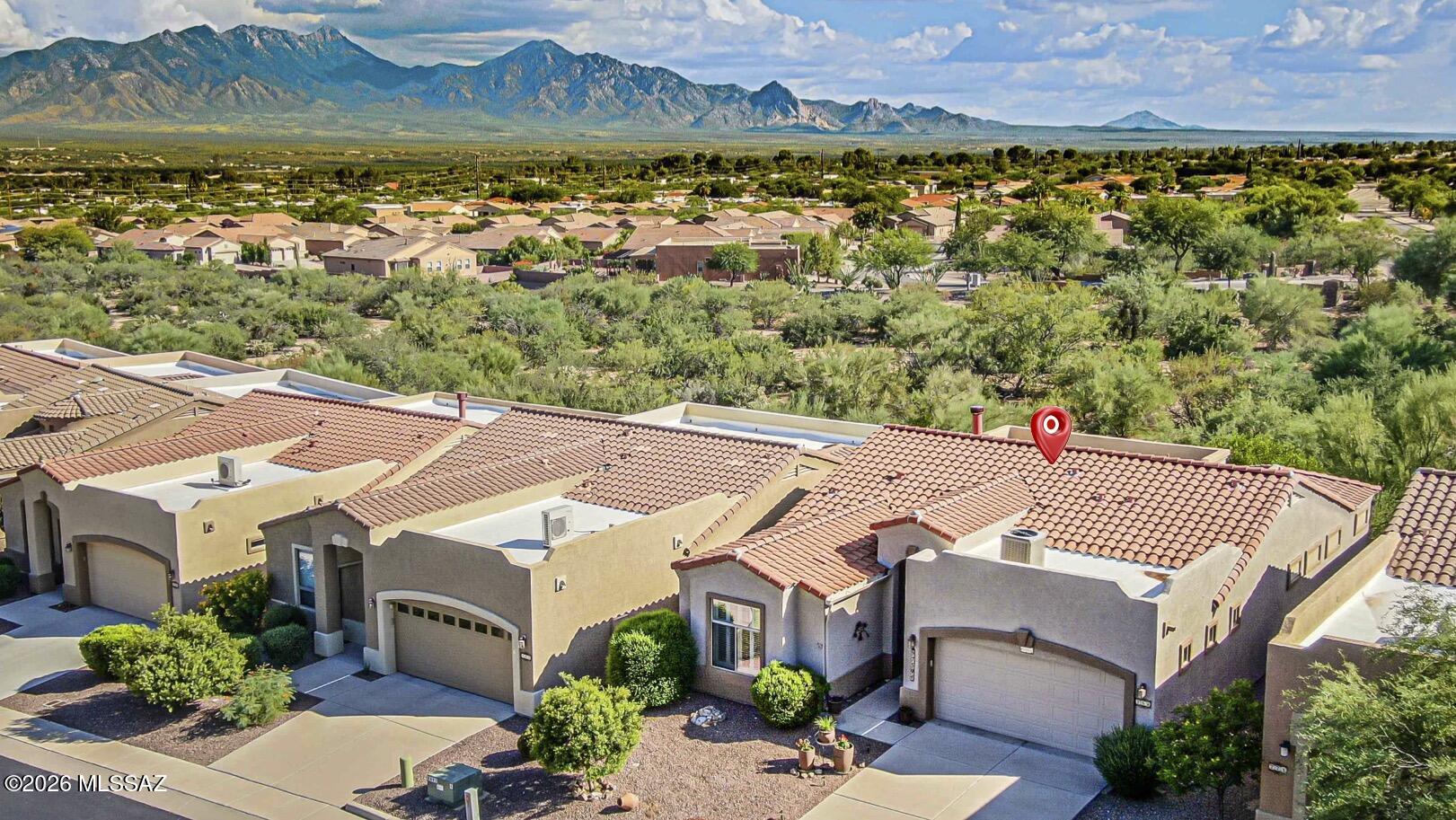 Aerial view of tile-roofed homes with a red location pin and mountains in the background.