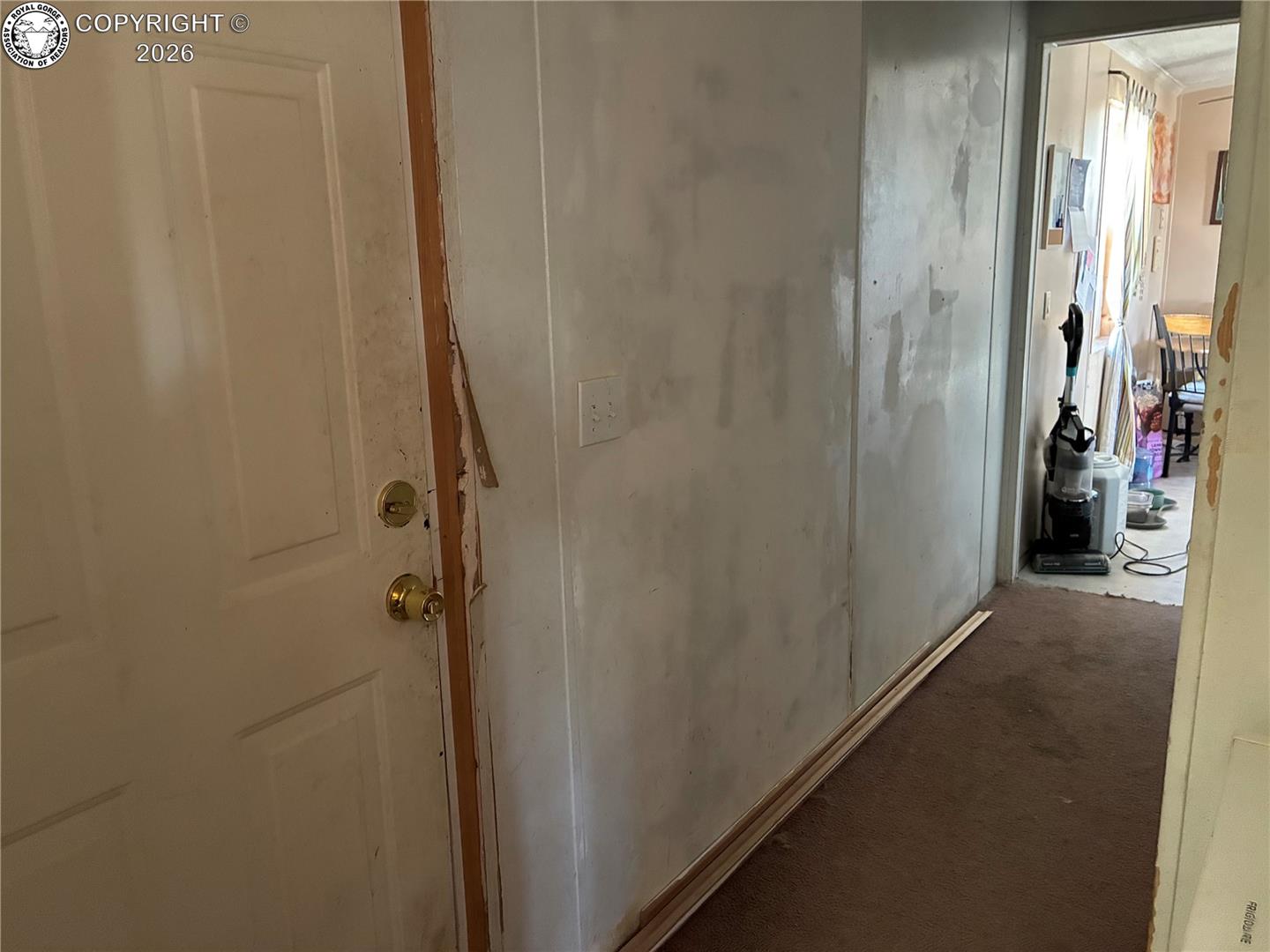 Hallway with unfinished drywall, loose baseboards, and a vacuum near the far doorway.