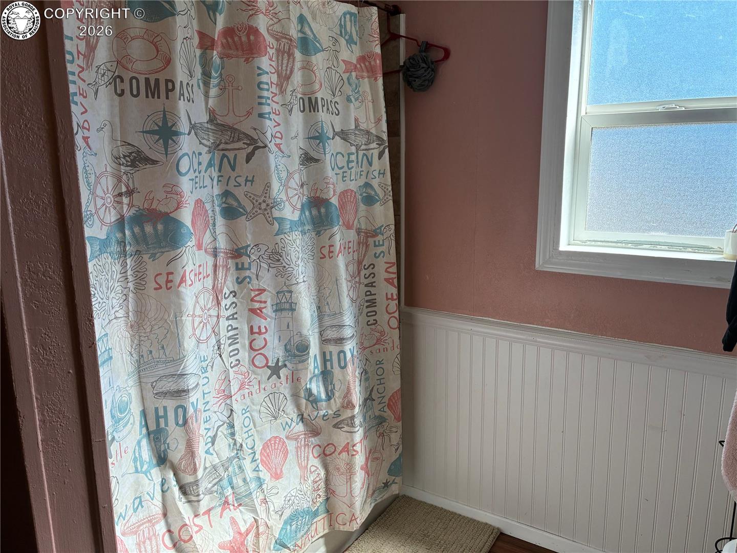 Bathroom with a colorful nautical-print shower curtain beside a frosted window and white beadboard wainscoting.