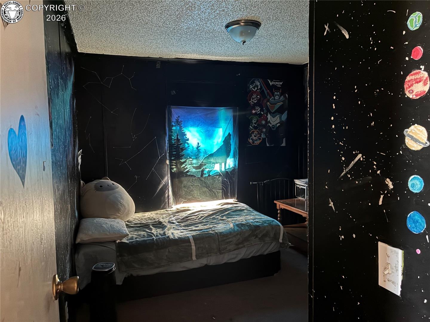 Bedroom with a bed, black space-themed walls, and a blue forest tapestry over the window.