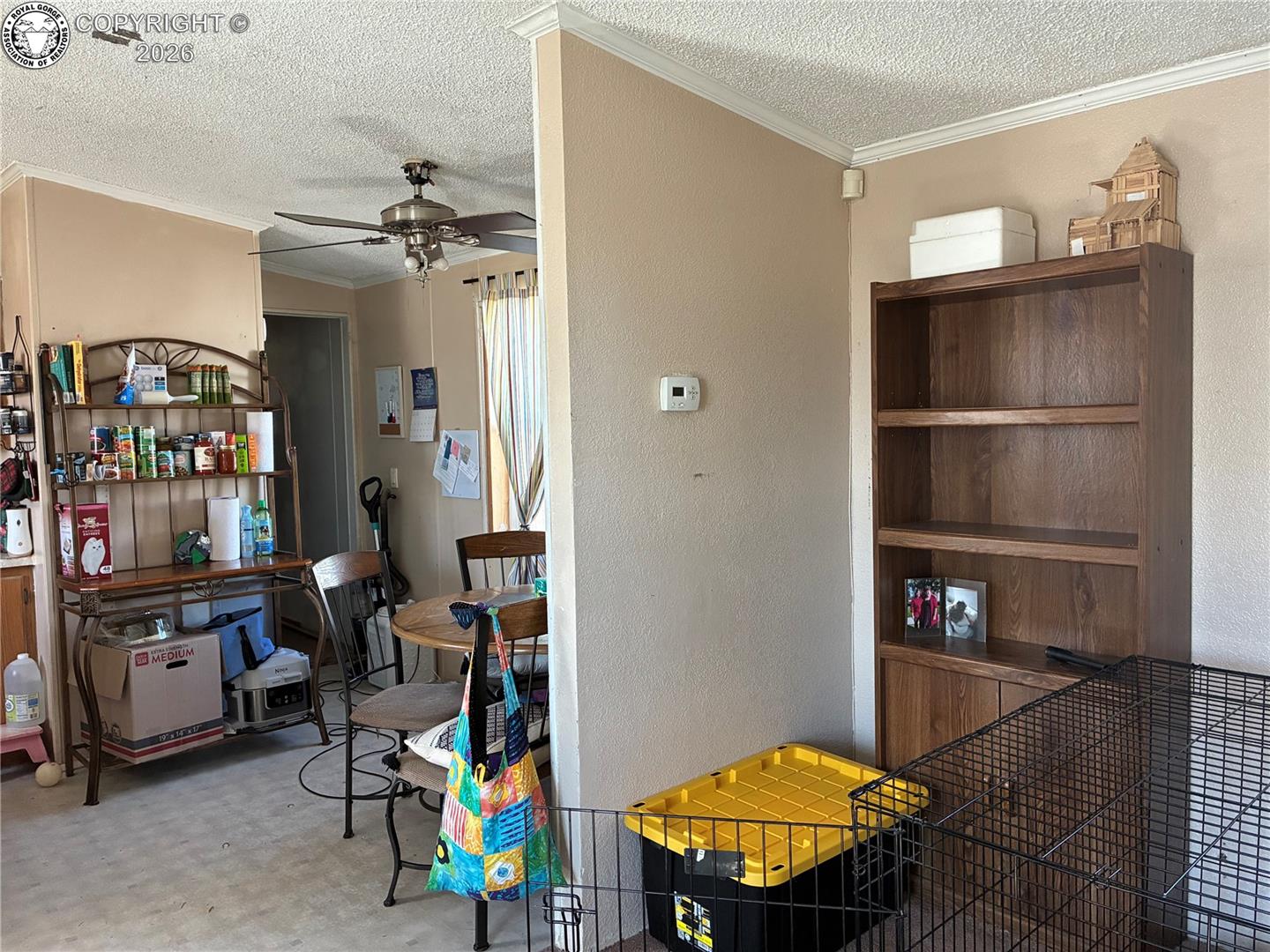 Dining area with a round table, stocked pantry shelf, wooden bookcase, and pet crate.