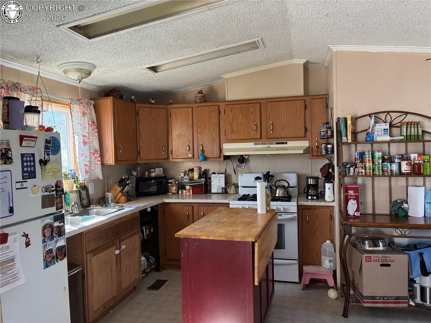 Kitchen with oak cabinets, a red island, white appliances, and crowded counters.