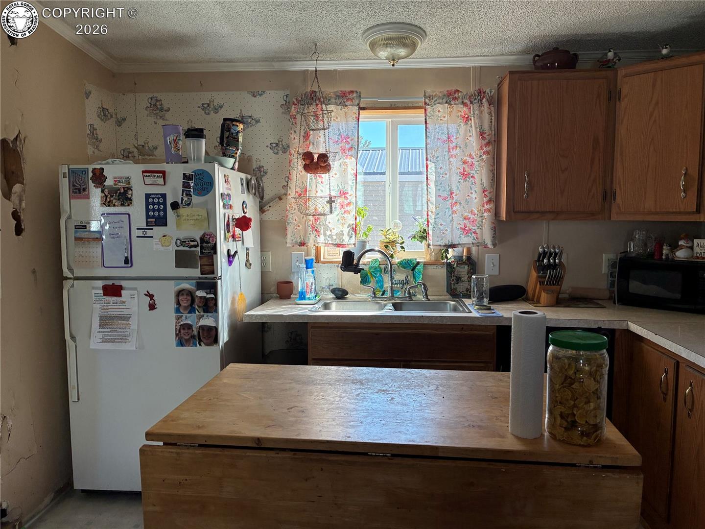 Kitchen with wooden cabinets, a large island, and a double sink beneath a floral-curtained window.