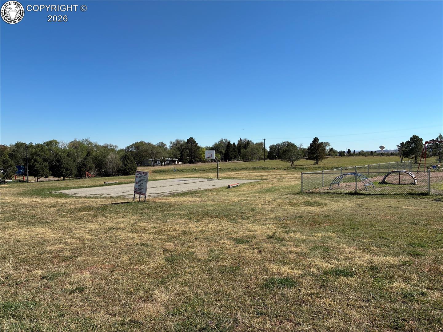 Community park with a basketball court and fenced playground in an open grassy field.