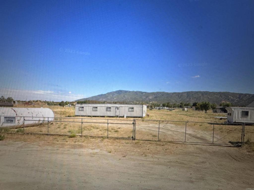 Fenced rural property with mobile homes, a white tank, and mountains in the background.