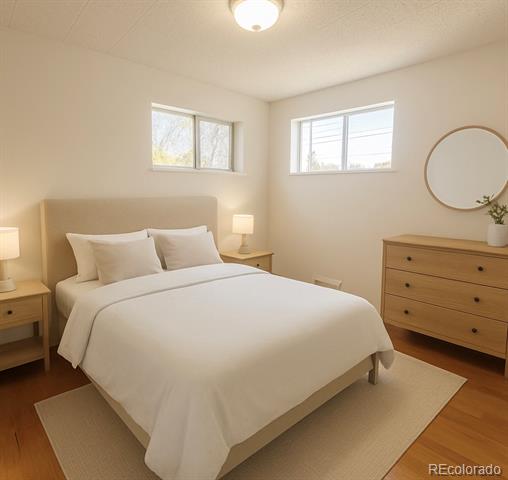 Staged bedroom with a white bed, two high windows, and a wooden dresser beneath a round mirror.