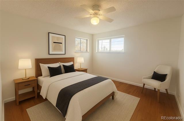 Furnished bedroom with white bedding, a dark bed runner, two windows, and a white accent chair.