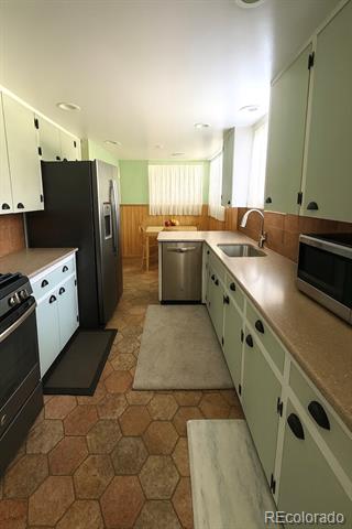 Galley kitchen with pale green cabinets, dark appliances, a central sink, and hexagonal tile flooring.