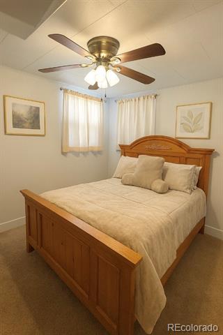 Bedroom with a wooden bed, cream bedding, ceiling fan, and two curtained corner windows.