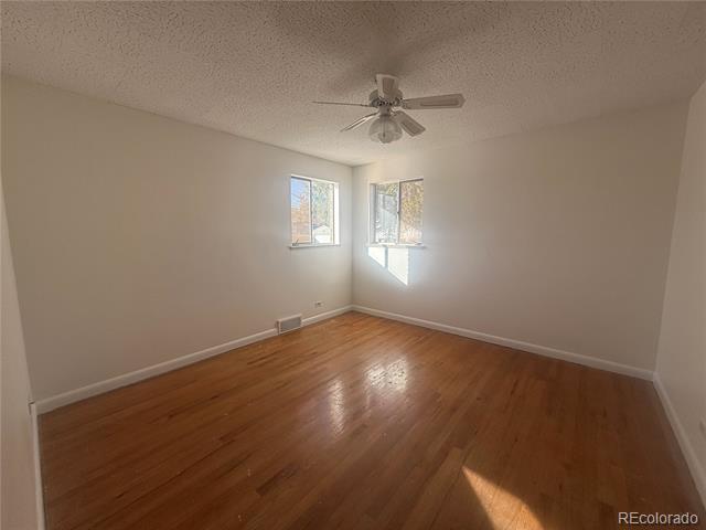 Empty room with polished hardwood floors, two corner windows, and a ceiling fan.