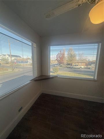 Empty room with dark flooring and two large windows with blinds.