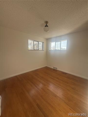 Empty room with hardwood floors, two windows, and a ceiling light.
