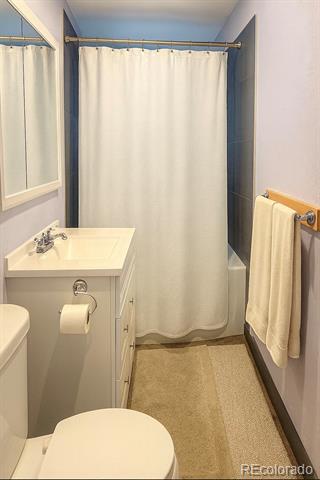 Bathroom with a white vanity, curtained tub or shower, and beige towels.
