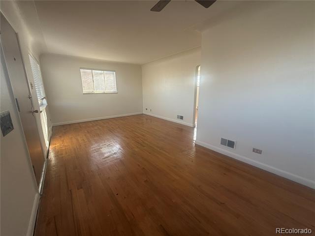Vacant room with polished hardwood floors, a window with blinds, and a ceiling fan.