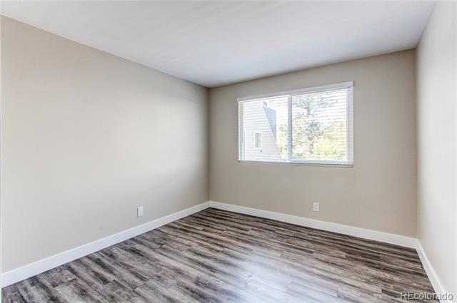 Empty bedroom with a window and dark wood-look flooring.
