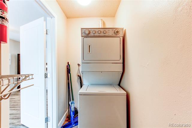 Laundry area with a stacked washer and dryer and cleaning tools stored beside them.