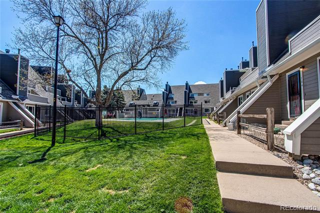 Condominium courtyard with a paved walkway, lawn, black metal fencing, and a leafless tree.