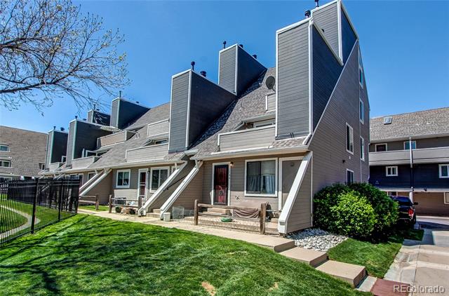 Multi-unit building with steep rooflines, gray siding, and a fenced lawn.