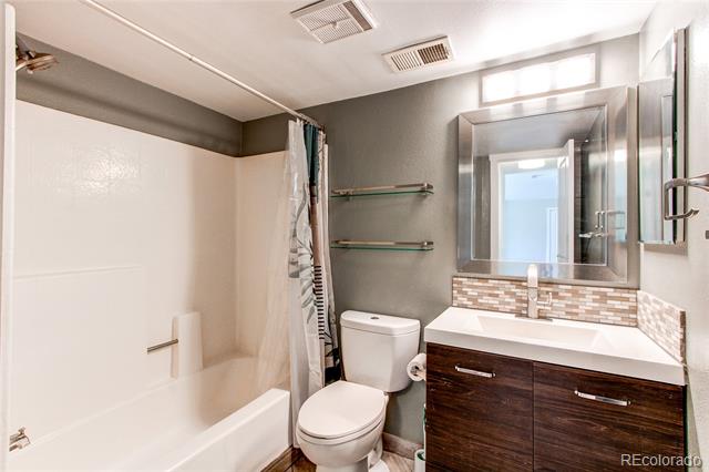 Bathroom with a white tub, toilet, dark wood vanity, and mosaic tile backsplash.
