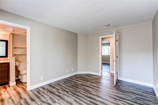 Empty bedroom with gray walls and wood-look flooring, adjoining a bathroom and hallway.