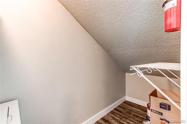 Storage area with a sloped ceiling, drying rack, and wood-look flooring.