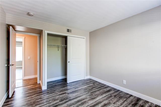 Empty bedroom with dark wood-look flooring and a partially open closet.