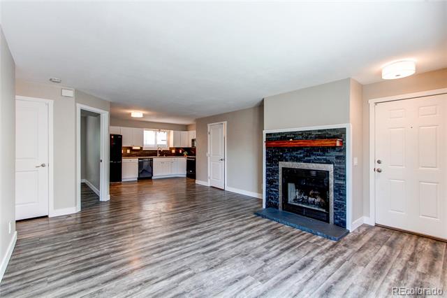 Condo living room with gray flooring, a tiled fireplace, and an open kitchen.