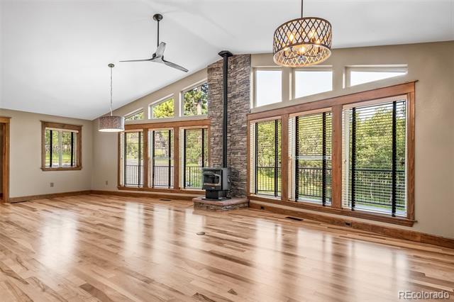 Vacant living room with hardwood floors, a stone-clad wood stove, and tall windows overlooking trees.