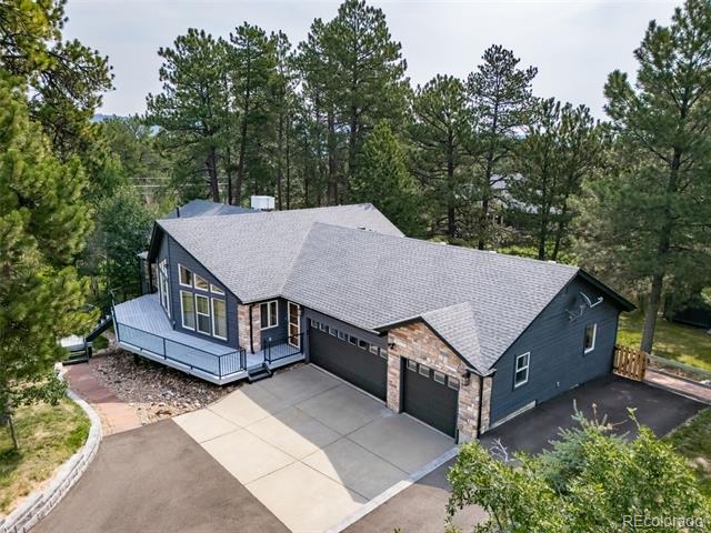 Single-story home with two garage doors, stone accents, and a raised deck among pine trees.
