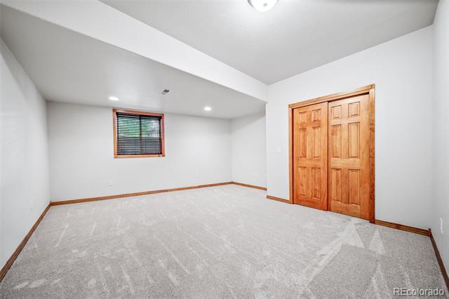 Empty bedroom with carpet, a small window with blinds, and wooden double closet doors.