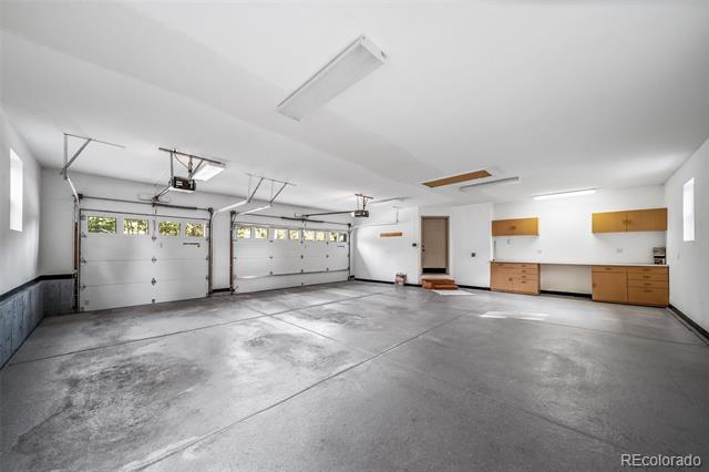 Two-car garage with white overhead doors, a concrete floor, and wooden cabinets along one wall.