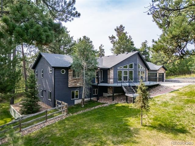 Dark-sided home with stone accents and raised deck among pine trees.