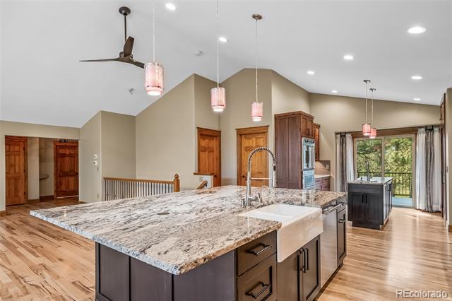 Open-plan kitchen with a granite island, farmhouse sink, dark cabinetry, and glass doors to a deck.