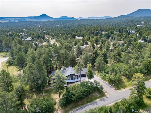 Aerial view of a wooded home with mountain ridges in the distance.