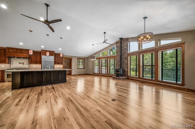 Open-plan living room and kitchen with hardwood floors, vaulted ceiling, large windows, and stone fireplace.