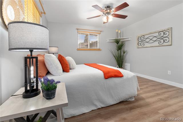 Bedroom with white bedding, orange accents, a bedside lamp, and wood-look flooring.