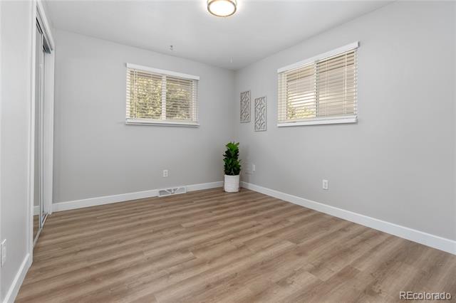 Unfurnished room with gray walls, two windows with blinds, and light wood flooring.