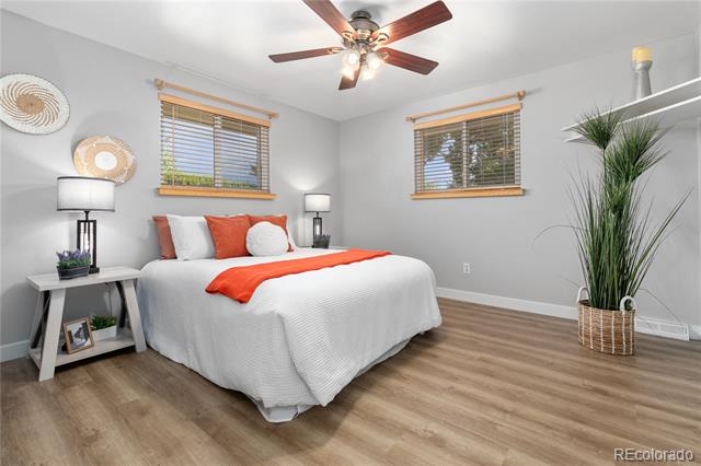 Staged bedroom with a white bed, orange accents, ceiling fan, and tall potted plant.