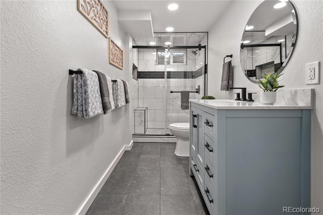 Bathroom with a blue-gray vanity and round mirror beside a glass-enclosed tiled shower.