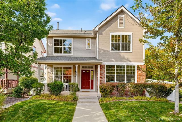 Two-story beige-and-brick home with a red front door, front walkway, and landscaped lawn.