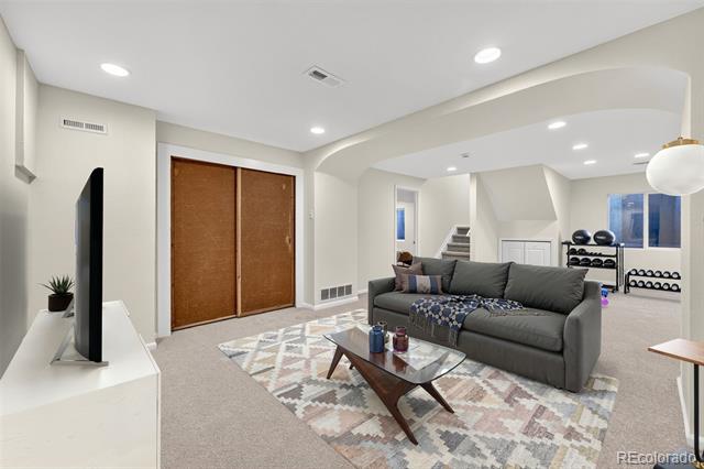Living room with gray sectional, patterned rug, glass coffee table, and exercise equipment nearby.