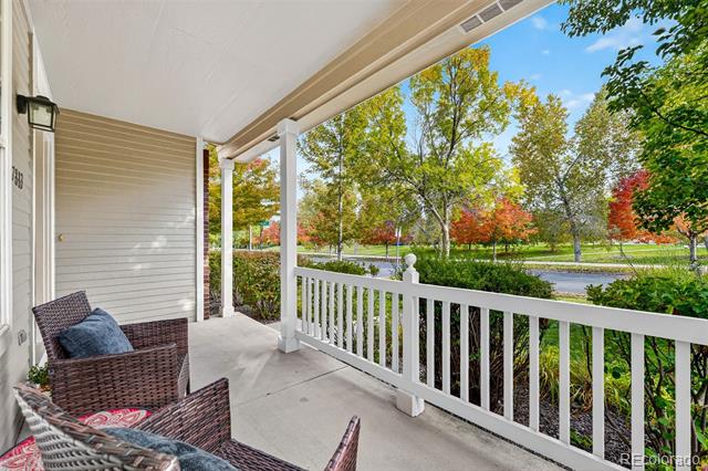 Covered porch with woven chairs and a white railing overlooking autumn trees along the street.