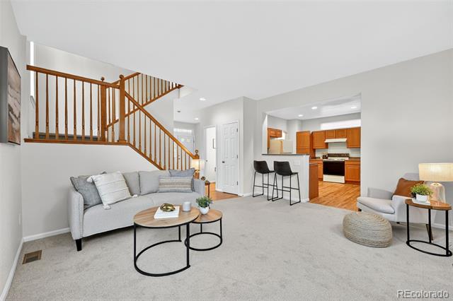 Staged living room with an open kitchen, wooden staircase, gray seating, and round coffee tables.