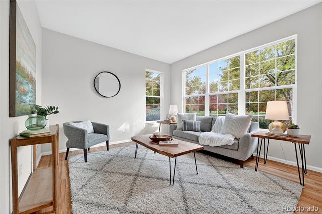 Staged living room with gray seating, a large light rug, and broad windows overlooking trees.