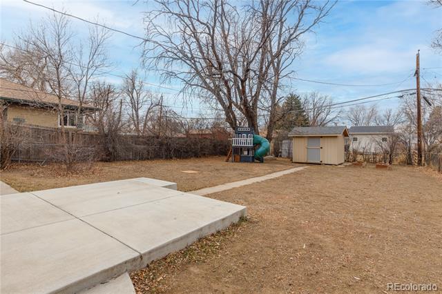 Backyard with a concrete patio, leafless trees, storage shed, and children's playset.