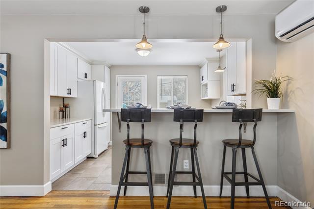 Kitchen with white cabinetry, a long breakfast bar, and three dark stools beneath pendant lights.