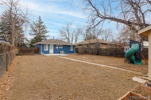 Fenced backyard with a concrete path, blue-sided house, and green tube slide.
