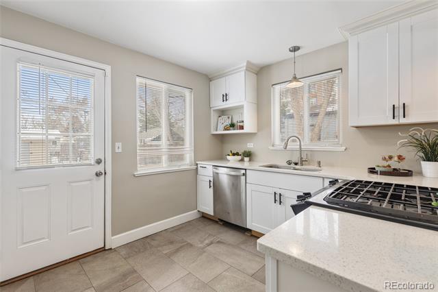 Bright kitchen with white cabinets, stainless appliances, and a stone island beside a glass-paneled door.
