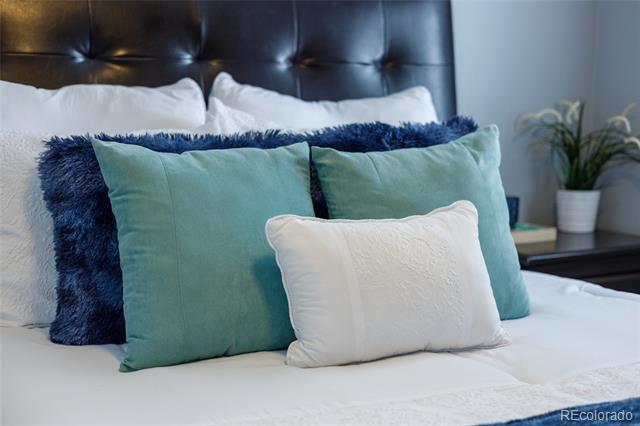 Bedroom bed with layered teal and navy pillows and a dark tufted headboard.